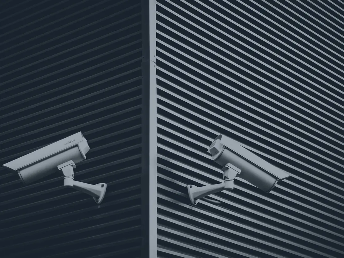 Two white bullet cameras mounted on a ribbed metal facade