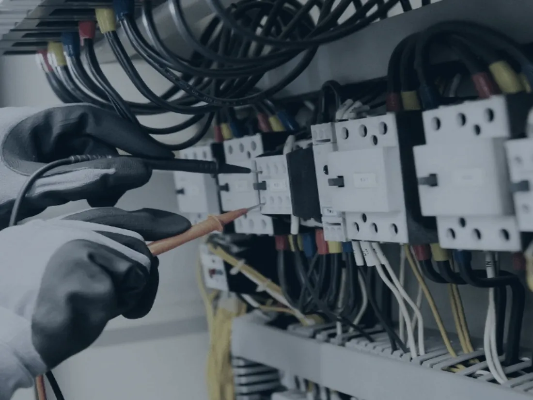A technician testing circuit breakers inside an electrical distribution board